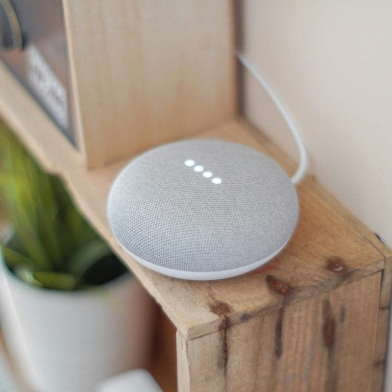 A Google Home Mini smart speaker on a wooden shelf, blending technology with home decor.